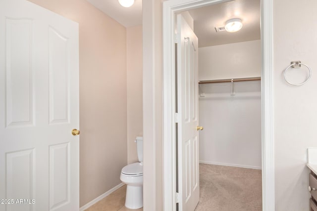 bathroom with visible vents, a spacious closet, toilet, vanity, and baseboards