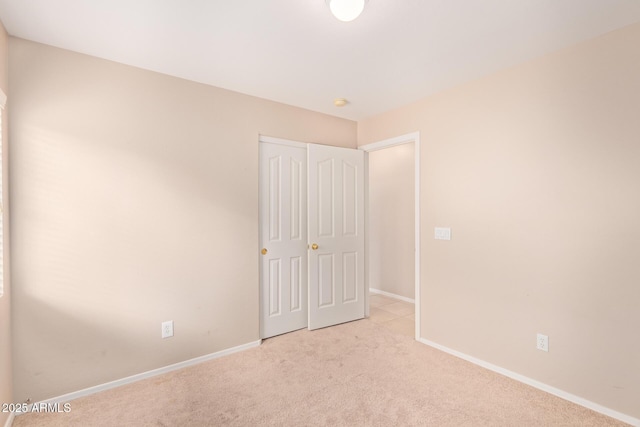 unfurnished bedroom featuring a closet, light carpet, and baseboards