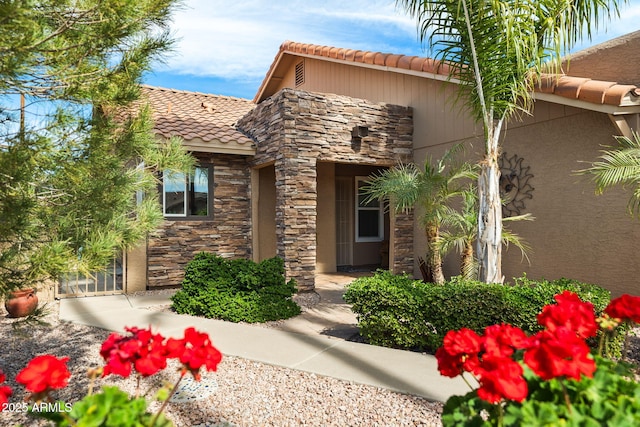 view of exterior entry featuring stone siding, a tile roof, and stucco siding