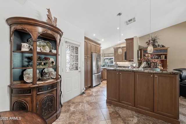 kitchen featuring visible vents, lofted ceiling, dark stone countertops, freestanding refrigerator, and decorative light fixtures