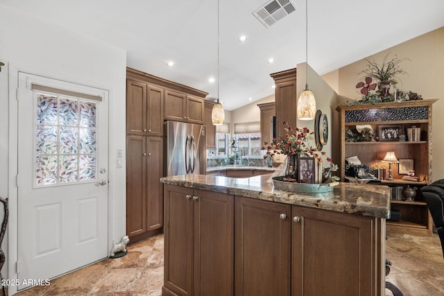 kitchen with stainless steel fridge, visible vents, lofted ceiling, dark stone countertops, and hanging light fixtures