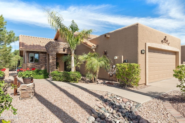 pueblo-style house with a garage, stone siding, a tile roof, and stucco siding