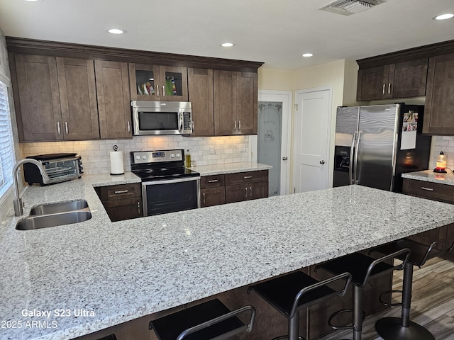 kitchen featuring stainless steel appliances, visible vents, a sink, and dark brown cabinets