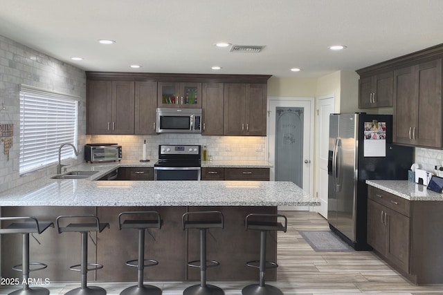 kitchen featuring dark brown cabinetry, stainless steel appliances, a peninsula, a sink, and visible vents