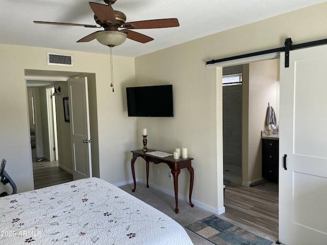 bedroom with ceiling fan, a barn door, wood finished floors, visible vents, and baseboards