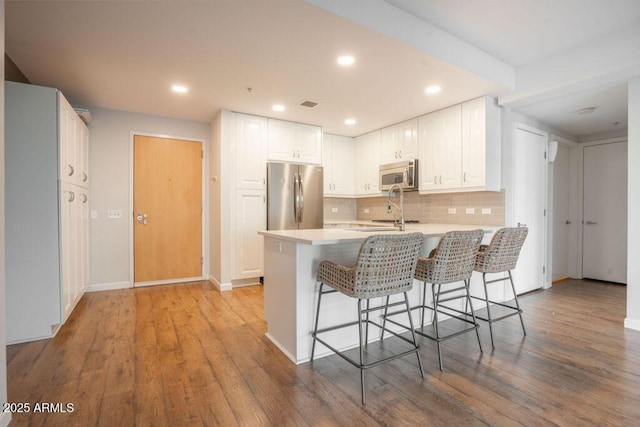 kitchen featuring light hardwood / wood-style flooring, backsplash, stainless steel appliances, a kitchen breakfast bar, and white cabinets