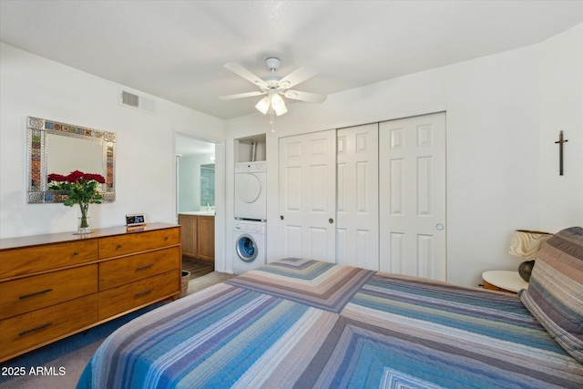 bedroom with visible vents, ceiling fan, stacked washer / drying machine, ensuite bathroom, and a closet