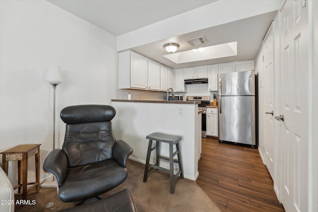 kitchen with under cabinet range hood, a peninsula, visible vents, white cabinets, and appliances with stainless steel finishes