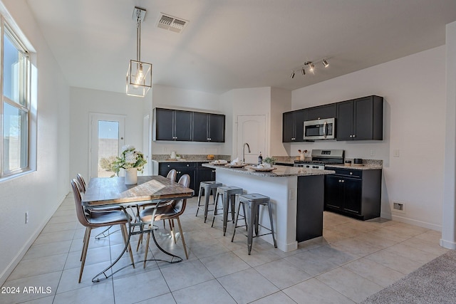 kitchen featuring light tile patterned floors, stainless steel appliances, hanging light fixtures, and an island with sink