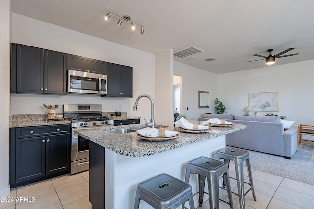 kitchen with sink, light stone countertops, an island with sink, appliances with stainless steel finishes, and a kitchen bar