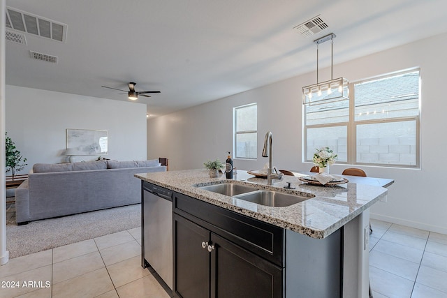 kitchen with light stone countertops, stainless steel dishwasher, a kitchen island with sink, sink, and pendant lighting