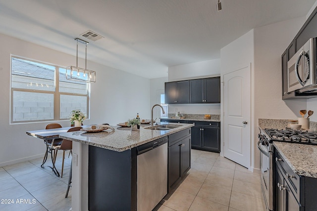 kitchen featuring light stone counters, stainless steel appliances, sink, decorative light fixtures, and a center island with sink