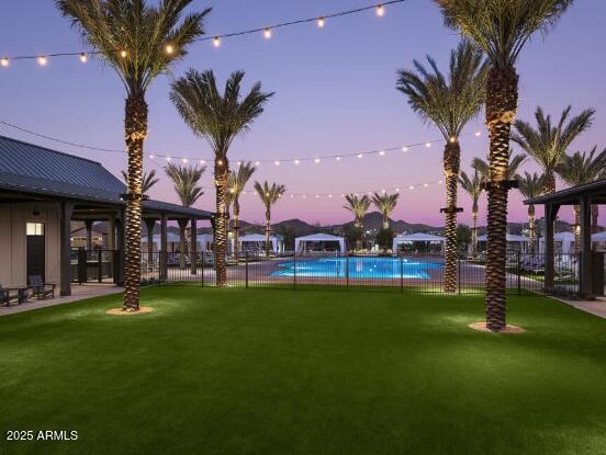 pool at dusk with a yard, a community pool, and fence