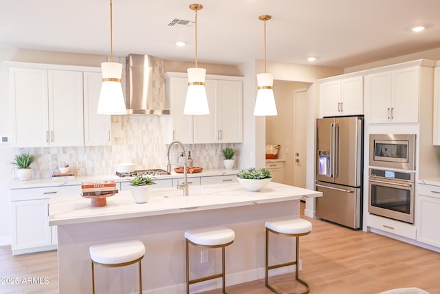 kitchen with white cabinets, wall chimney exhaust hood, stainless steel appliances, and decorative light fixtures