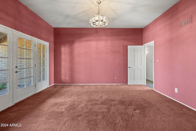 carpeted spare room featuring a chandelier and french doors