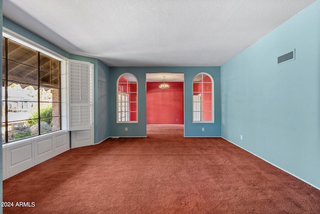 carpeted empty room with a textured ceiling and an inviting chandelier