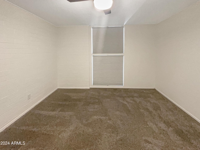 spare room featuring ceiling fan, brick wall, and dark colored carpet