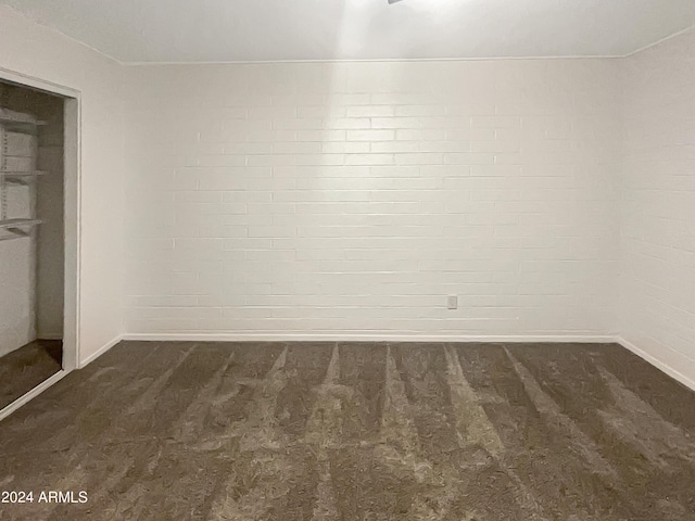 empty room featuring brick wall and dark carpet