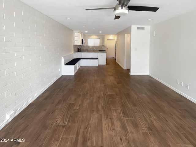 unfurnished living room featuring dark wood-type flooring, ceiling fan, brick wall, and sink