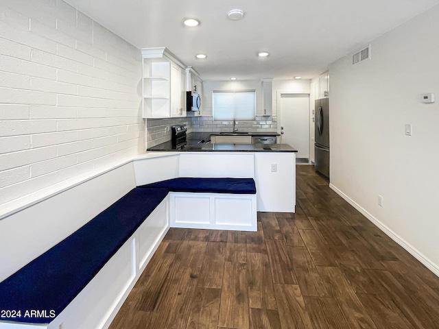 kitchen with dark wood-type flooring, appliances with stainless steel finishes, white cabinets, decorative backsplash, and kitchen peninsula