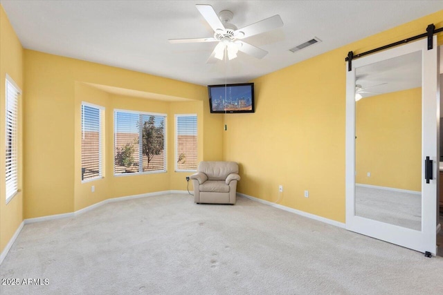 unfurnished room featuring ceiling fan, a barn door, and light colored carpet