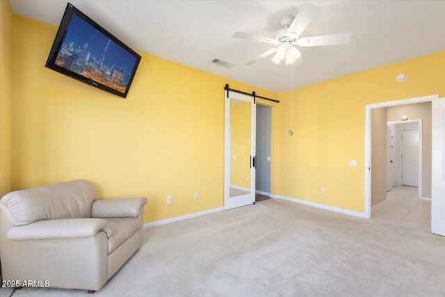 living area featuring ceiling fan, a barn door, and light colored carpet