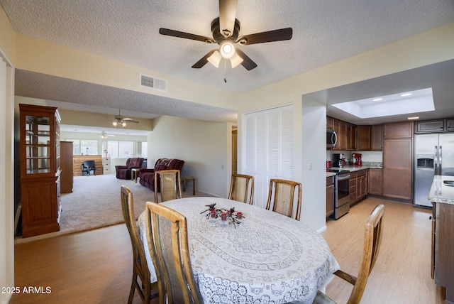 dining area with ceiling fan, a tray ceiling, light hardwood / wood-style flooring, and a textured ceiling