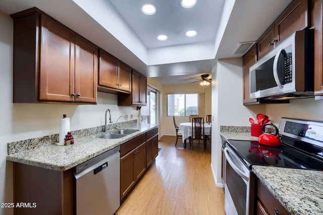 kitchen with sink, stainless steel appliances, light hardwood / wood-style floors, and light stone countertops