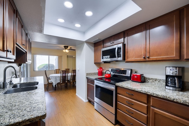 kitchen with sink, appliances with stainless steel finishes, light stone counters, light hardwood / wood-style floors, and a raised ceiling