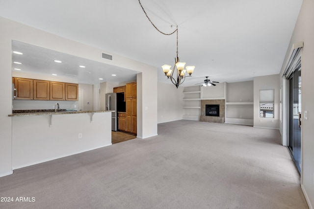 unfurnished living room featuring built in features, sink, a fireplace, light carpet, and ceiling fan with notable chandelier