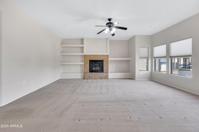 unfurnished living room featuring light carpet, ceiling fan, built in shelves, and a tile fireplace