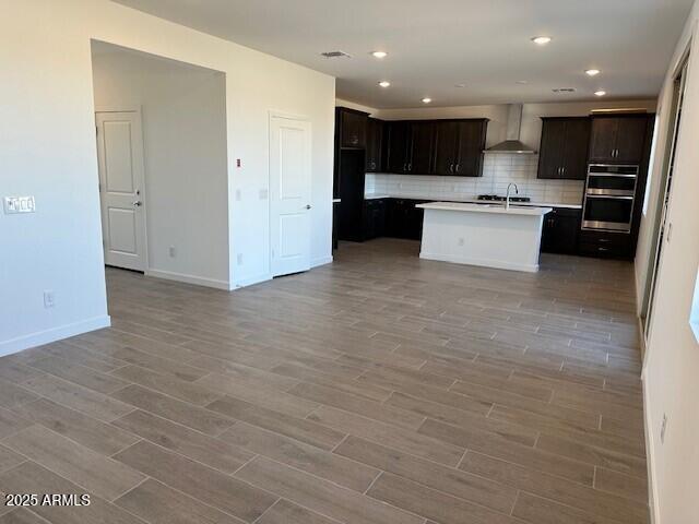 kitchen featuring backsplash, wall chimney range hood, double oven, light wood-style floors, and a sink