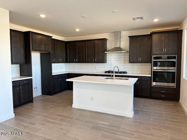 kitchen featuring wood finish floors, stainless steel appliances, wall chimney exhaust hood, and light countertops