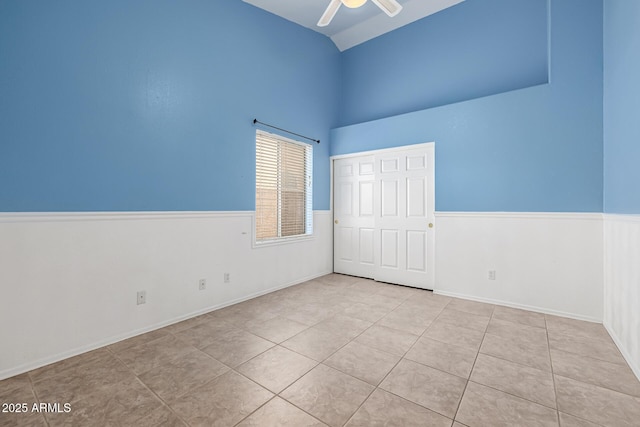 spare room featuring tile patterned floors, wainscoting, a ceiling fan, and vaulted ceiling