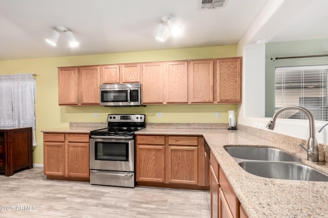 kitchen with light stone counters, appliances with stainless steel finishes, sink, and light hardwood / wood-style flooring