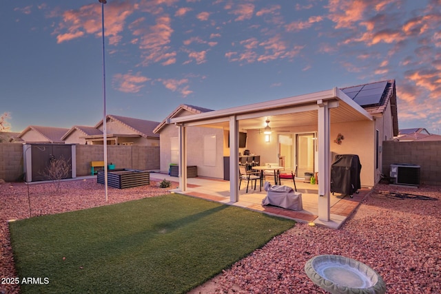 back house at dusk featuring solar panels, a lawn, a patio area, and central air condition unit