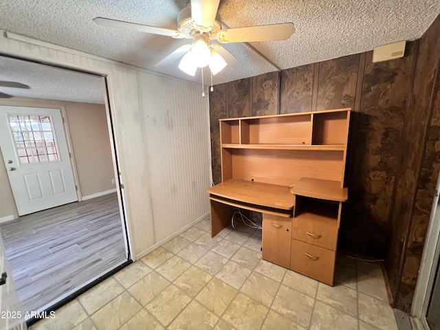 unfurnished office featuring wooden walls, a ceiling fan, and a textured ceiling