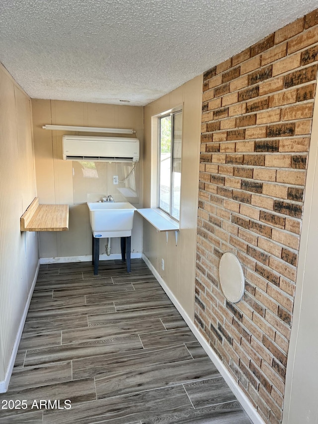 interior space with a sink, a textured ceiling, wood finished floors, a wall mounted air conditioner, and baseboards