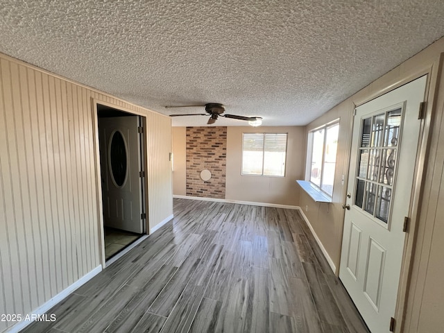 spare room featuring wood walls, a textured ceiling, baseboards, and wood finished floors