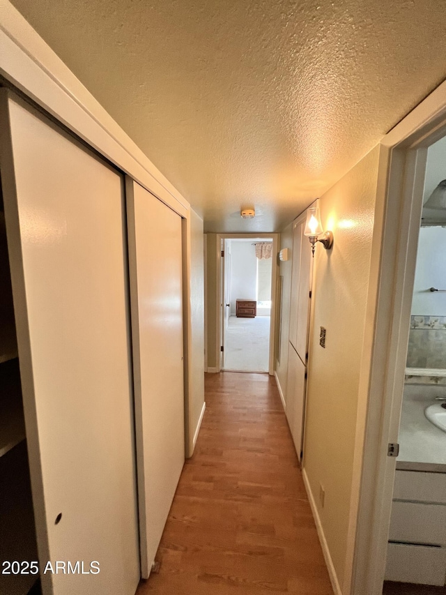 corridor featuring a textured ceiling, baseboards, and light wood-style floors