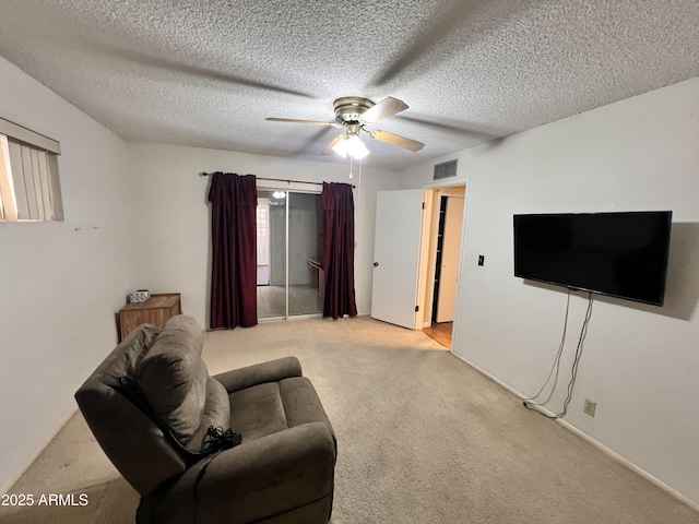 carpeted living room with a textured ceiling, visible vents, and a ceiling fan