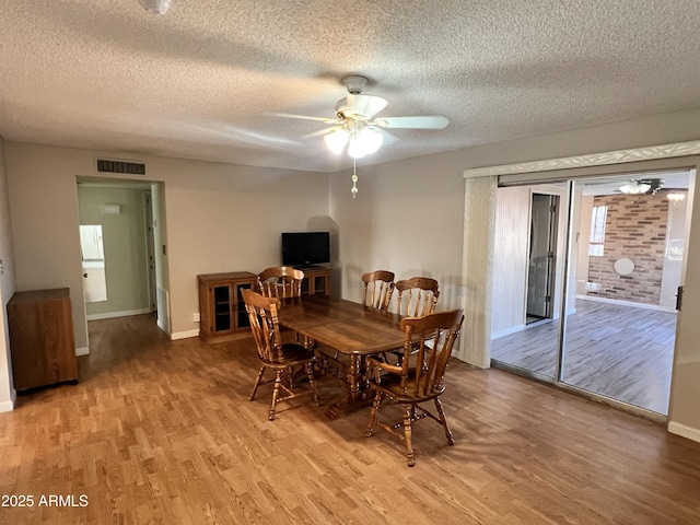 dining area featuring light wood finished floors, ceiling fan, visible vents, and a textured ceiling