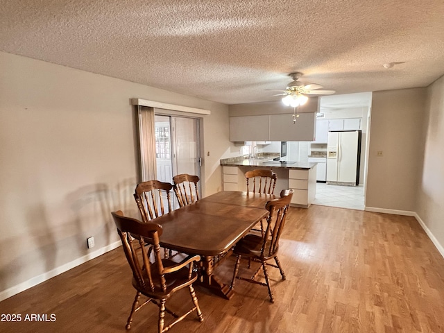 dining area featuring light wood-style flooring, baseboards, ceiling fan, and a textured ceiling