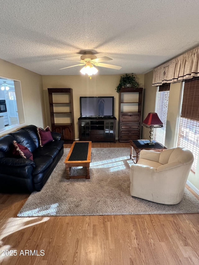 living room with a ceiling fan, a textured ceiling, and wood finished floors