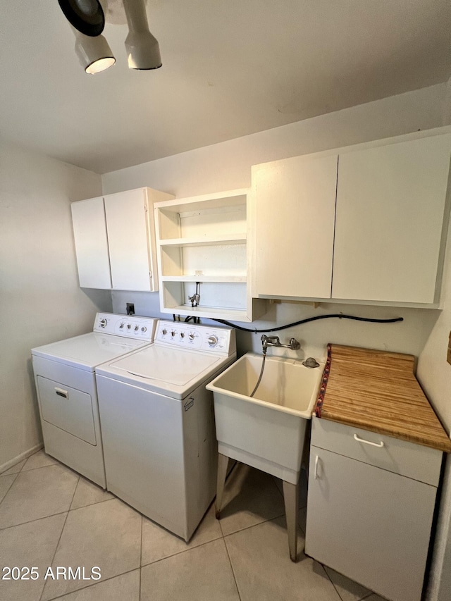 clothes washing area with cabinet space, washing machine and dryer, light tile patterned floors, and a sink