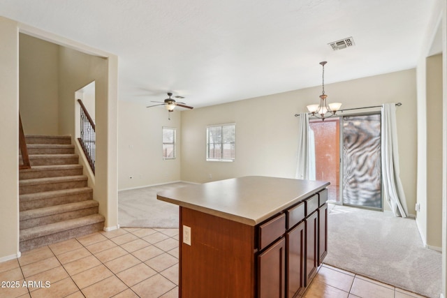 kitchen with light colored carpet, decorative light fixtures, ceiling fan with notable chandelier, and a kitchen island