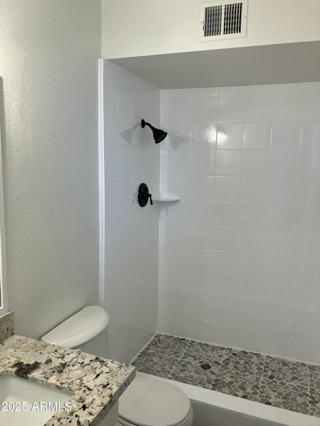 bathroom featuring toilet, vanity, and tiled shower