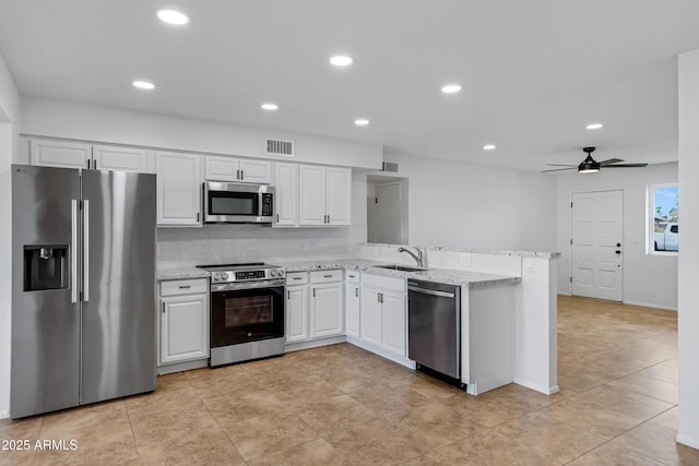 kitchen featuring white cabinetry, stainless steel appliances, tasteful backsplash, light stone countertops, and kitchen peninsula