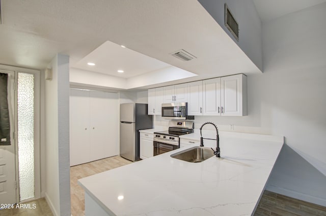 kitchen featuring white cabinetry, sink, stainless steel appliances, kitchen peninsula, and light wood-type flooring