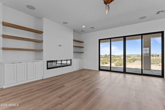 34198 S State Route 89th Hwy, Wickenburg, AZ 85390 - unfurnished living room with a glass covered fireplace, light wood-type flooring, built in shelves, and baseboards